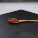 Wooden spoon with paprika on black slate board.