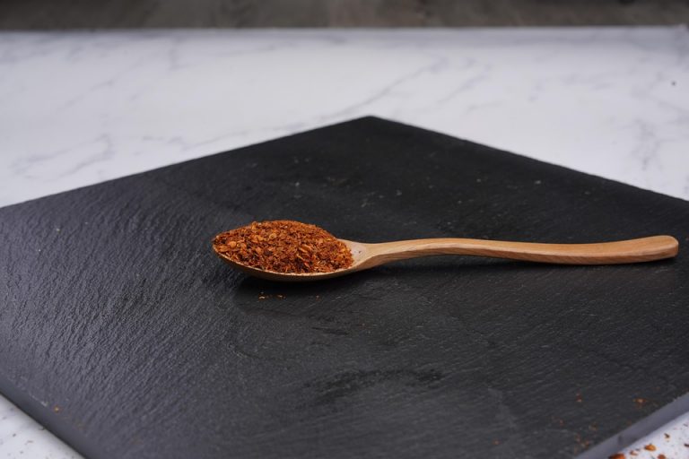 Wooden spoon with paprika on black slate board.