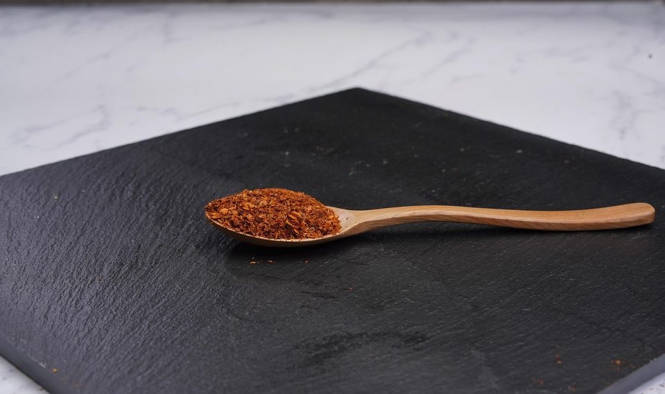 Wooden spoon with paprika on black slate board.
