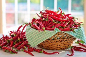Basket overflowing with fresh red chili peppers on table.