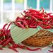 Basket overflowing with fresh red chili peppers on table.