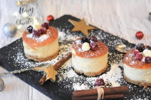 Festive mini cheesecakes with berries and powdered sugar on a slate platter.
