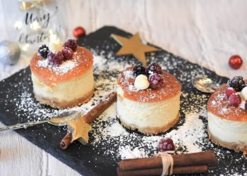 Festive mini cheesecakes with berries and powdered sugar on a slate platter.