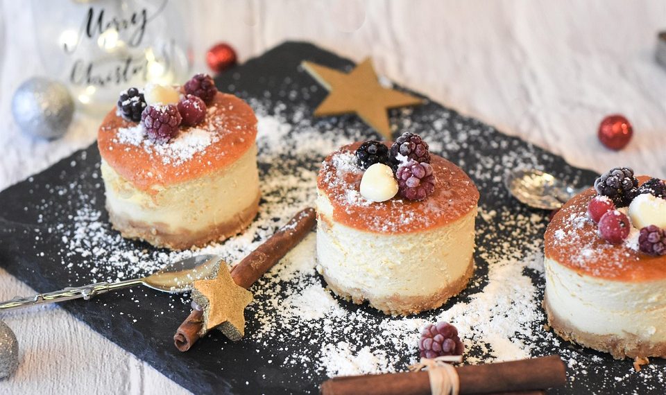 Festive mini cheesecakes with berries and powdered sugar on a slate platter.