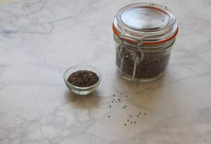 Jar and bowl of chia seeds on marble surface.