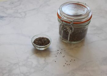 Jar and bowl of chia seeds on marble surface.