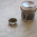 Jar and bowl of chia seeds on marble surface.