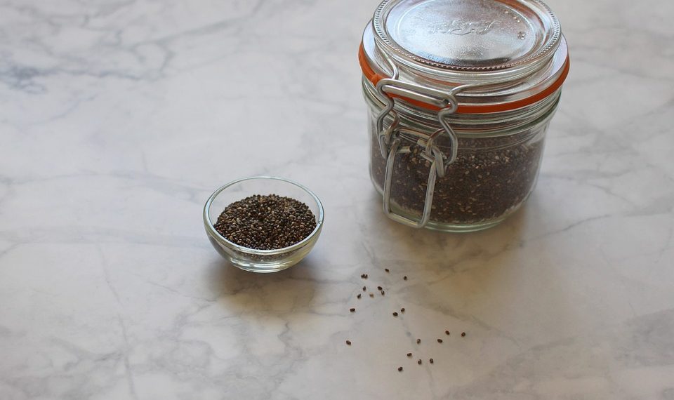 Jar and bowl of chia seeds on marble surface.