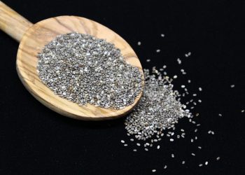 Chia seeds spilling from wooden spoon on black background.