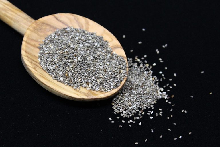 Chia seeds spilling from wooden spoon on black background.