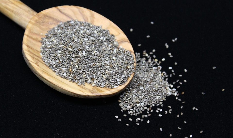 Chia seeds spilling from wooden spoon on black background.