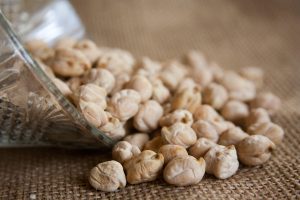 Chickpeas spilling from a glass jar onto a burlap surface.