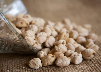 Chickpeas spilling from a glass jar onto a burlap surface.