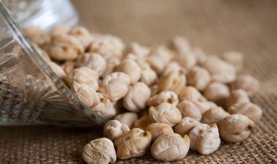 Chickpeas spilling from a glass jar onto a burlap surface.