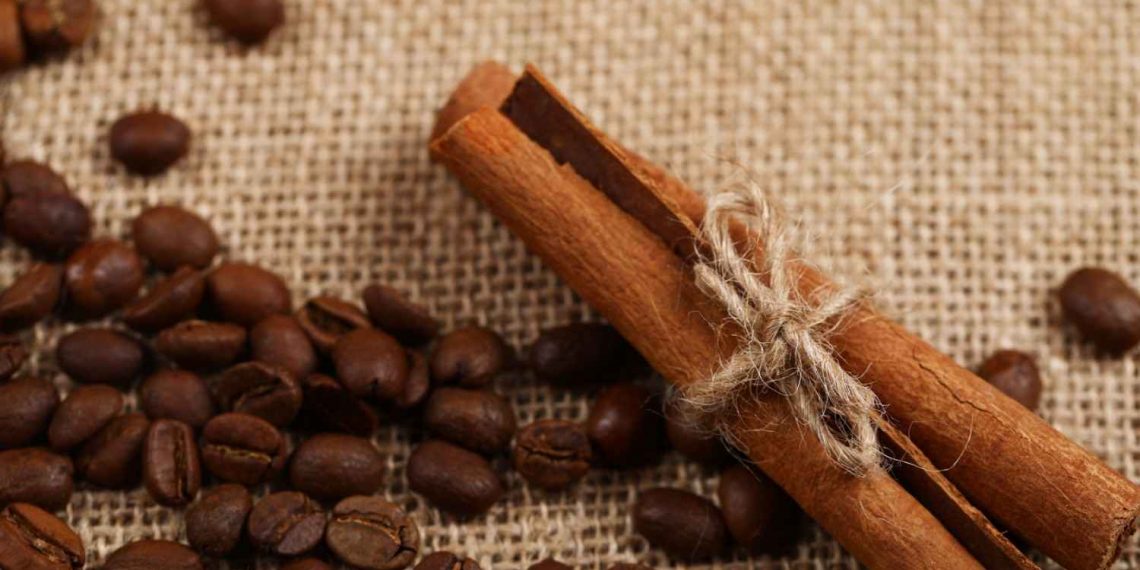 Cinnamon sticks tied with twine beside coffee beans on burlap.