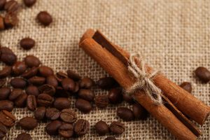 Cinnamon sticks tied with twine beside coffee beans on burlap.