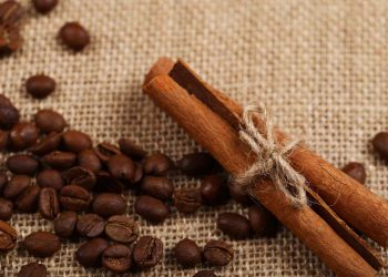 Cinnamon sticks tied with twine beside coffee beans on burlap.