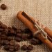 Cinnamon sticks tied with twine beside coffee beans on burlap.