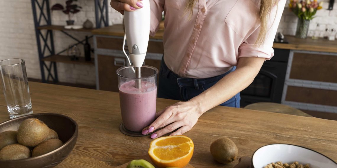 Blending fruit smoothie with immersion blender on wooden counter.