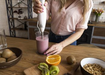 Blending fruit smoothie with immersion blender on wooden counter.