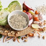 Fresh vegetables and nuts on a table with a bowl of quinoa.