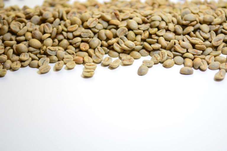 Unroasted coffee beans scattered on white background.