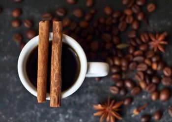 Cup of coffee with cinnamon sticks surrounded by coffee beans.