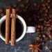 Cup of coffee with cinnamon sticks surrounded by coffee beans.