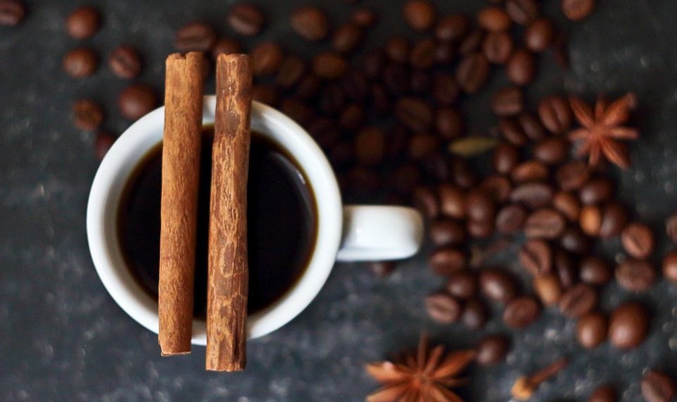 Cup of coffee with cinnamon sticks surrounded by coffee beans.