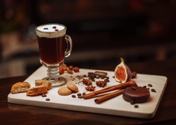 Creamy coffee with assorted pastries and spices on a wooden tray.