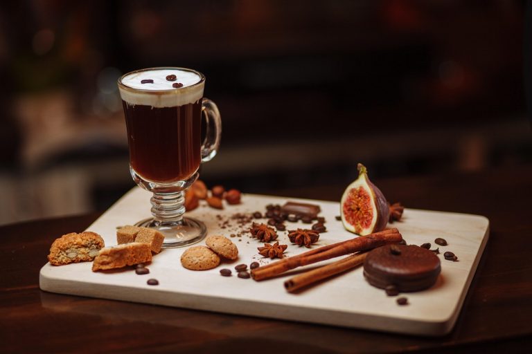 Creamy coffee with assorted pastries and spices on a wooden tray.