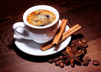 Steaming coffee with cinnamon sticks and star anise on a wooden table.