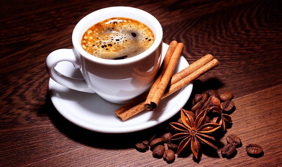 Steaming coffee with cinnamon sticks and star anise on a wooden table.
