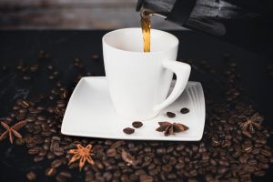 Pouring coffee into a white cup surrounded by coffee beans.