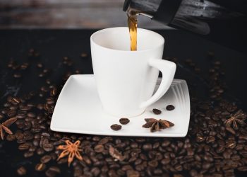 Pouring coffee into a white cup surrounded by coffee beans.