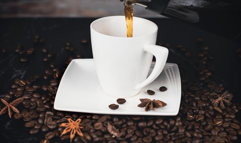 Pouring coffee into a white cup surrounded by coffee beans.