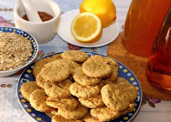 Oatmeal cookies on a plate with lemons and honey ingredients.
