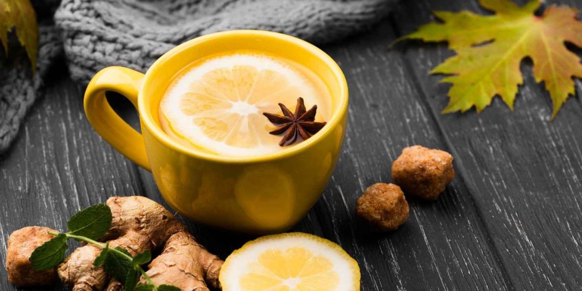 Yellow mug with lemon ginger tea, star anise on dark table.