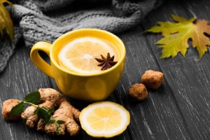 Yellow mug with lemon ginger tea, star anise on dark table.