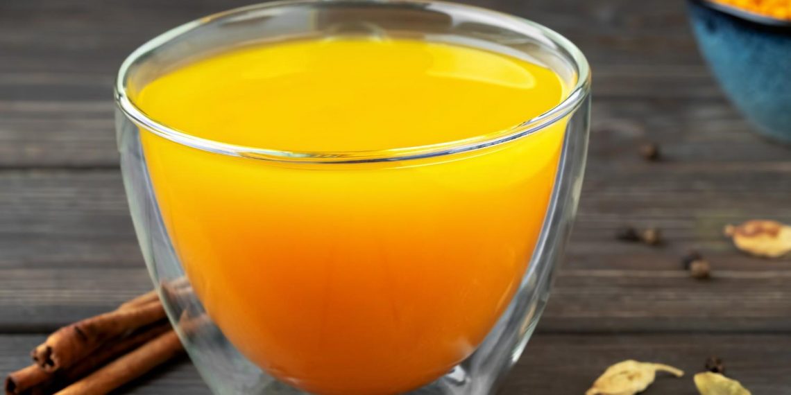 Warm turmeric tea with spices on wooden table.