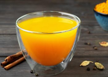 Warm turmeric tea with spices on wooden table.