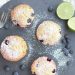 Blueberry muffins with powdered sugar on slate, limes and blueberries on side.