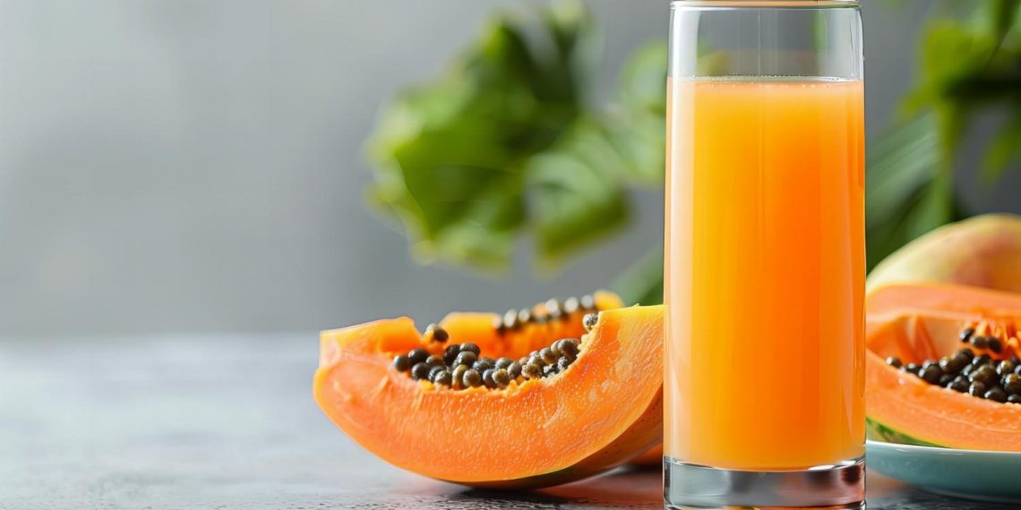 Fresh papaya juice in a glass with sliced papaya on table.