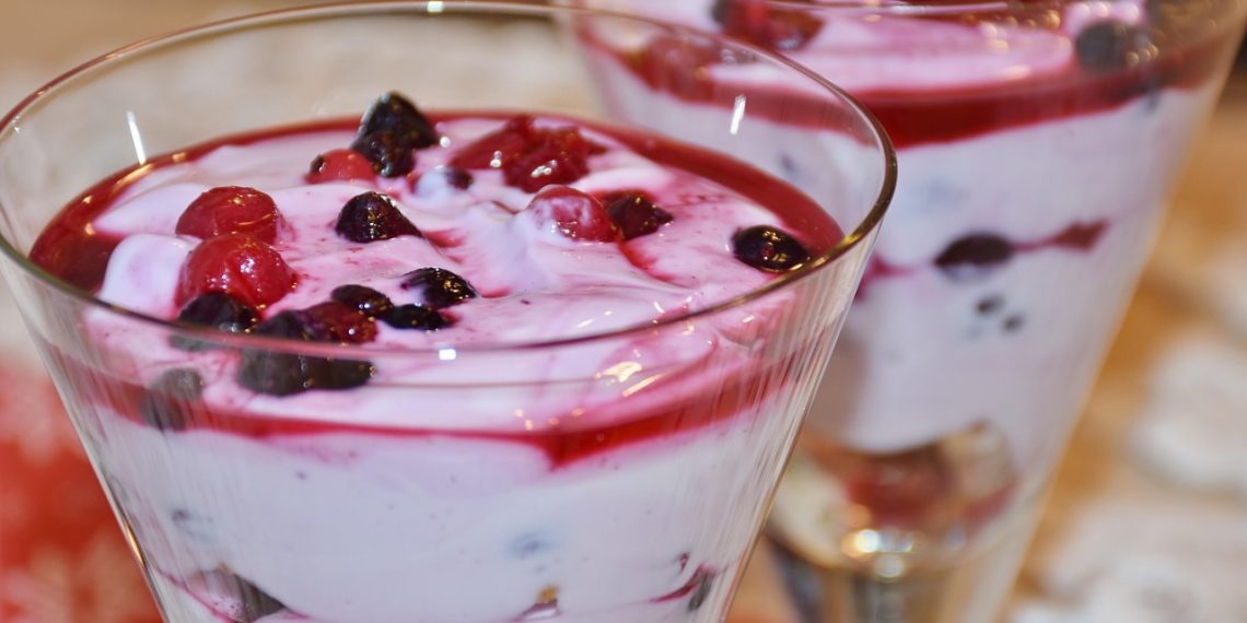 A delicious dessert in a glass, featuring creamy yogurt topped with mixed berries and a vibrant berry sauce.