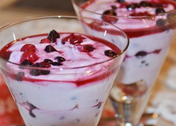 A delicious dessert in a glass, featuring creamy yogurt topped with mixed berries and a vibrant berry sauce.