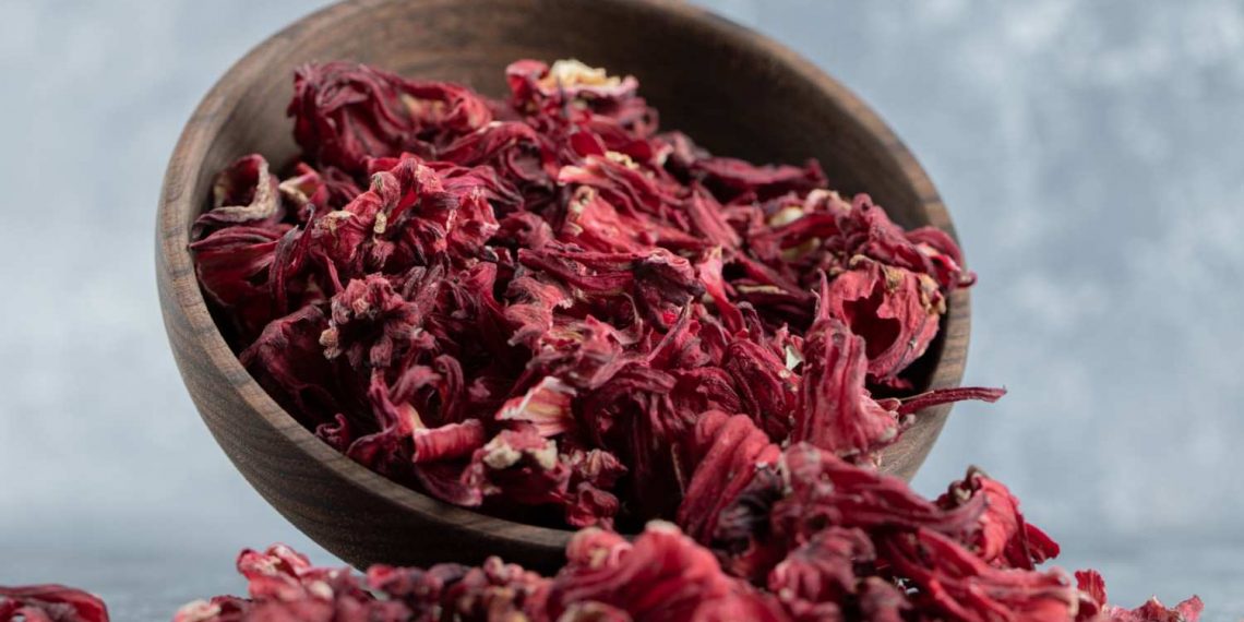 Dried hibiscus petals spilling from a wooden bowl.