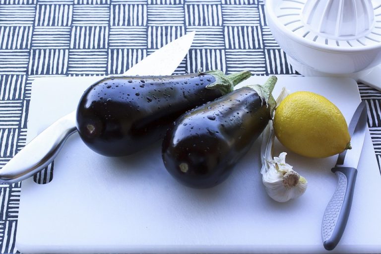 Eggplants, lemon, and garlic on a cutting board with knives.