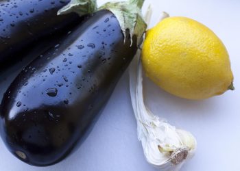 Eggplants with water droplets beside a lemon and garlic.