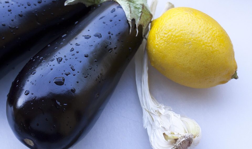 Eggplants with water droplets beside a lemon and garlic.