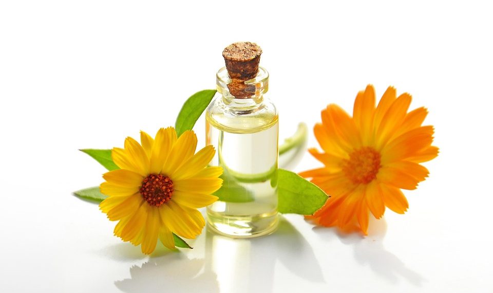 Oil bottle with calendula flowers on white background.